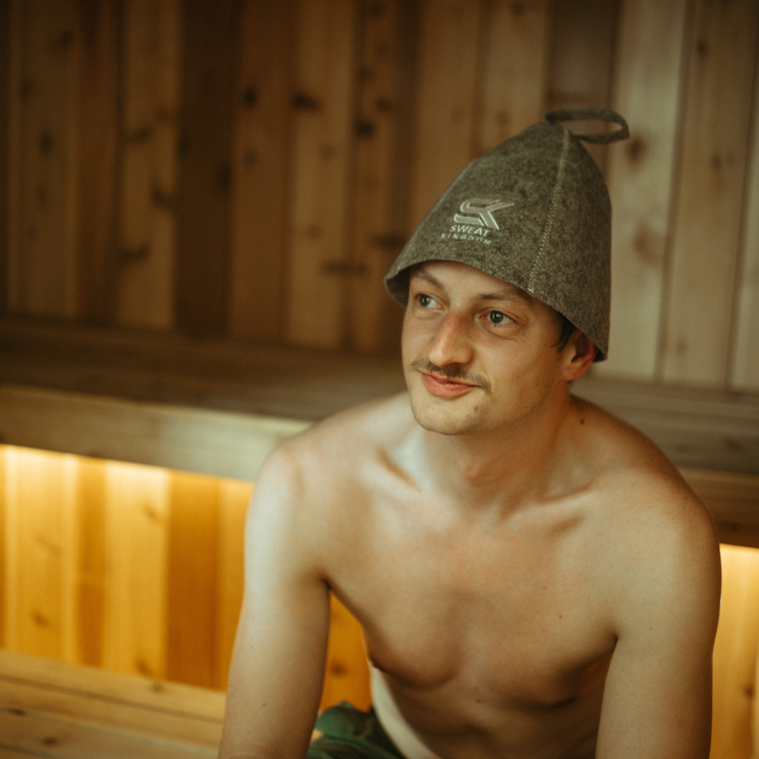 Man wearing a traditional Finnish sauna hat in a wooden sauna.