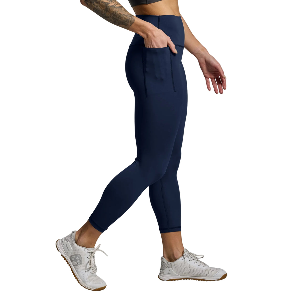 Person wearing navy leggings and white sneakers on a gray background