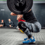 Person lifting a barbell in a gym setting with other people in the background.
