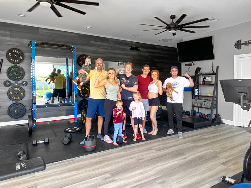 Family posing together in a home gym with exercise equipment and a TV.