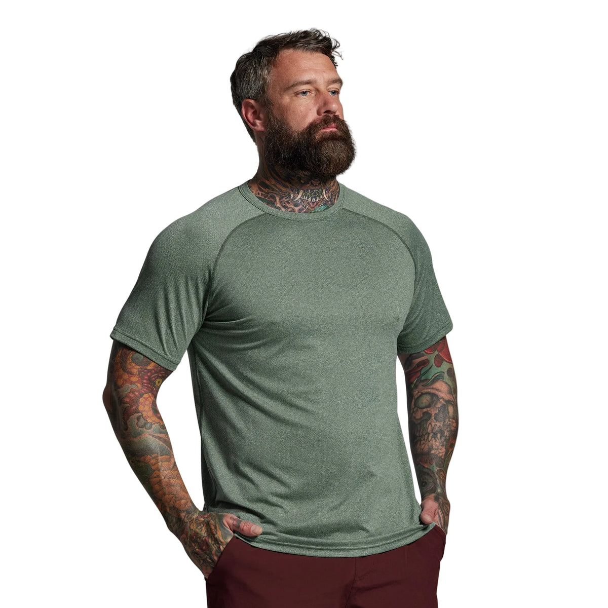 Man wearing a green t-shirt with tattoos on his arms against a gray background