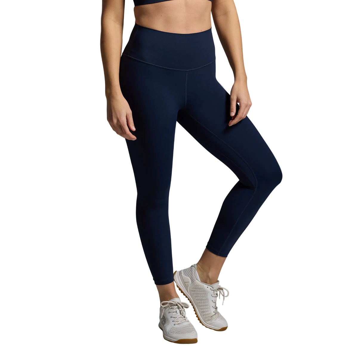 Person wearing navy leggings and white sneakers on a gray background