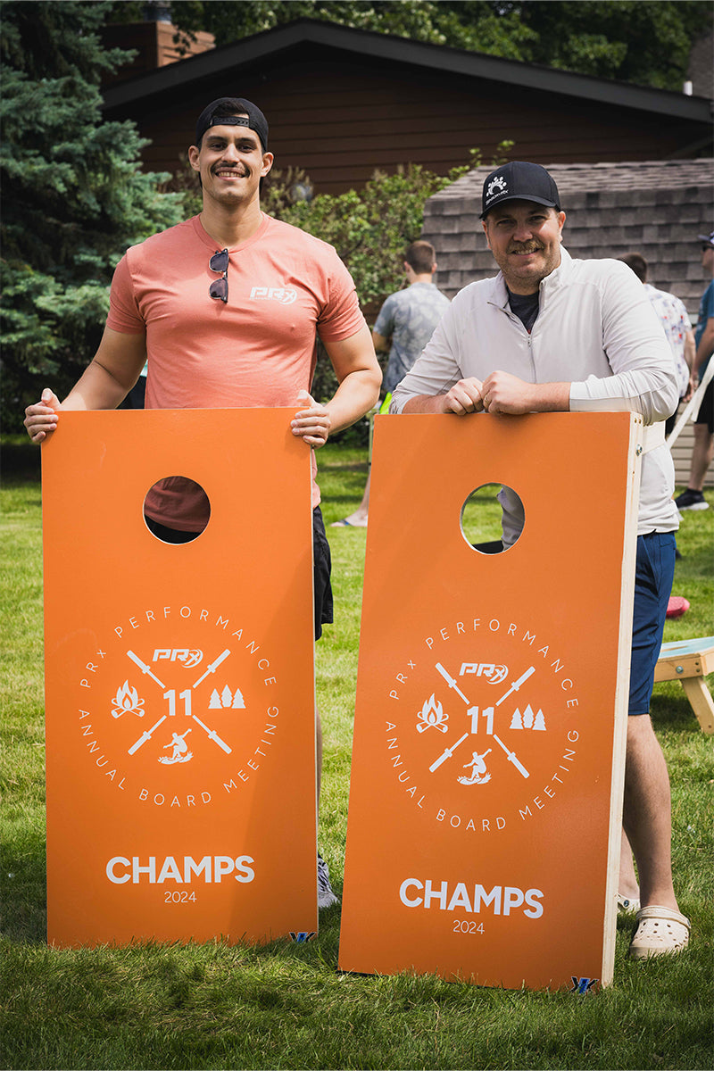 Two PRx Employees smiling holding cornhole boards during 2024 board meeting