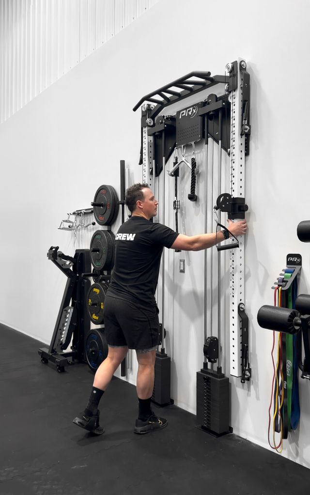 man folding up a white PRx Squat Rack with cable system on a white wall