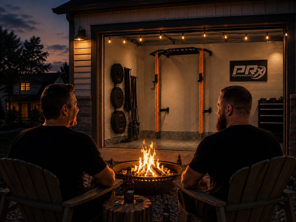 Two men sitting in wooden Adirondack chairs facing a lit fire pit, with a home gym visible inside an open garage behind them at dusk. A garage door sign reads PR Performance.