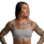 Woman wearing a gray sports bra with tattoos on her arms and chest against a plain background