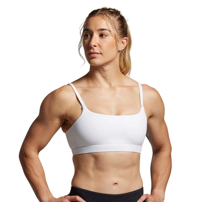Woman wearing a white sports bra and black leggings on a gray background