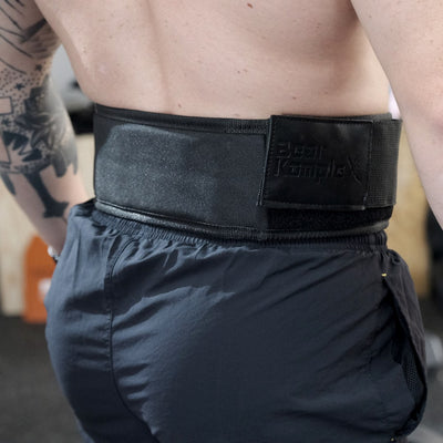 Person wearing a black weightlifting belt with visible branding in an indoor setting.