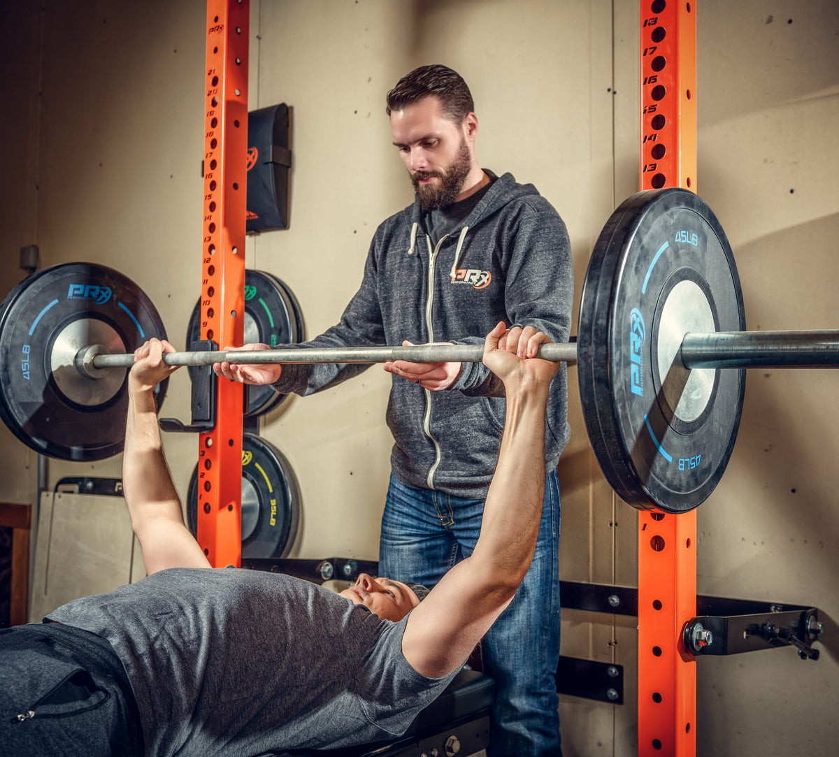 two men bench pressing inside of a folding squat rack in a garage