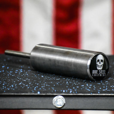 Metal cylindrical object with a skull logo on a black surface with an American flag in the background